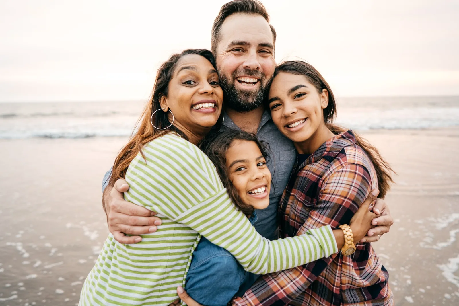 Two adults and two children smiling and embracing on a beach.