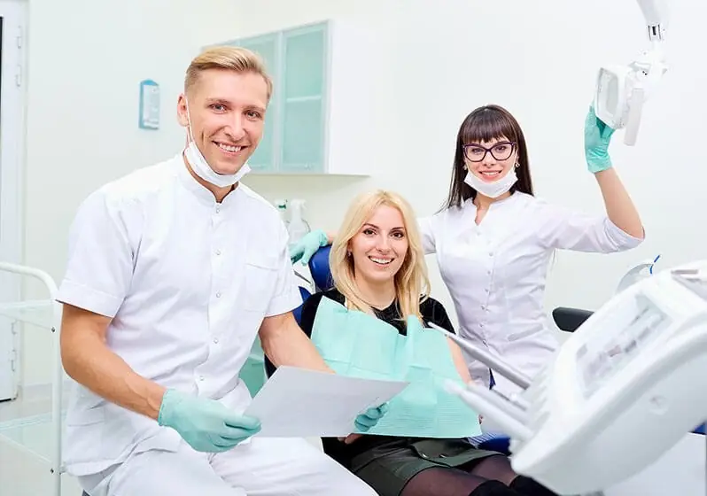 Two dental professionals smiling alongside a patient seated in a dental chair.