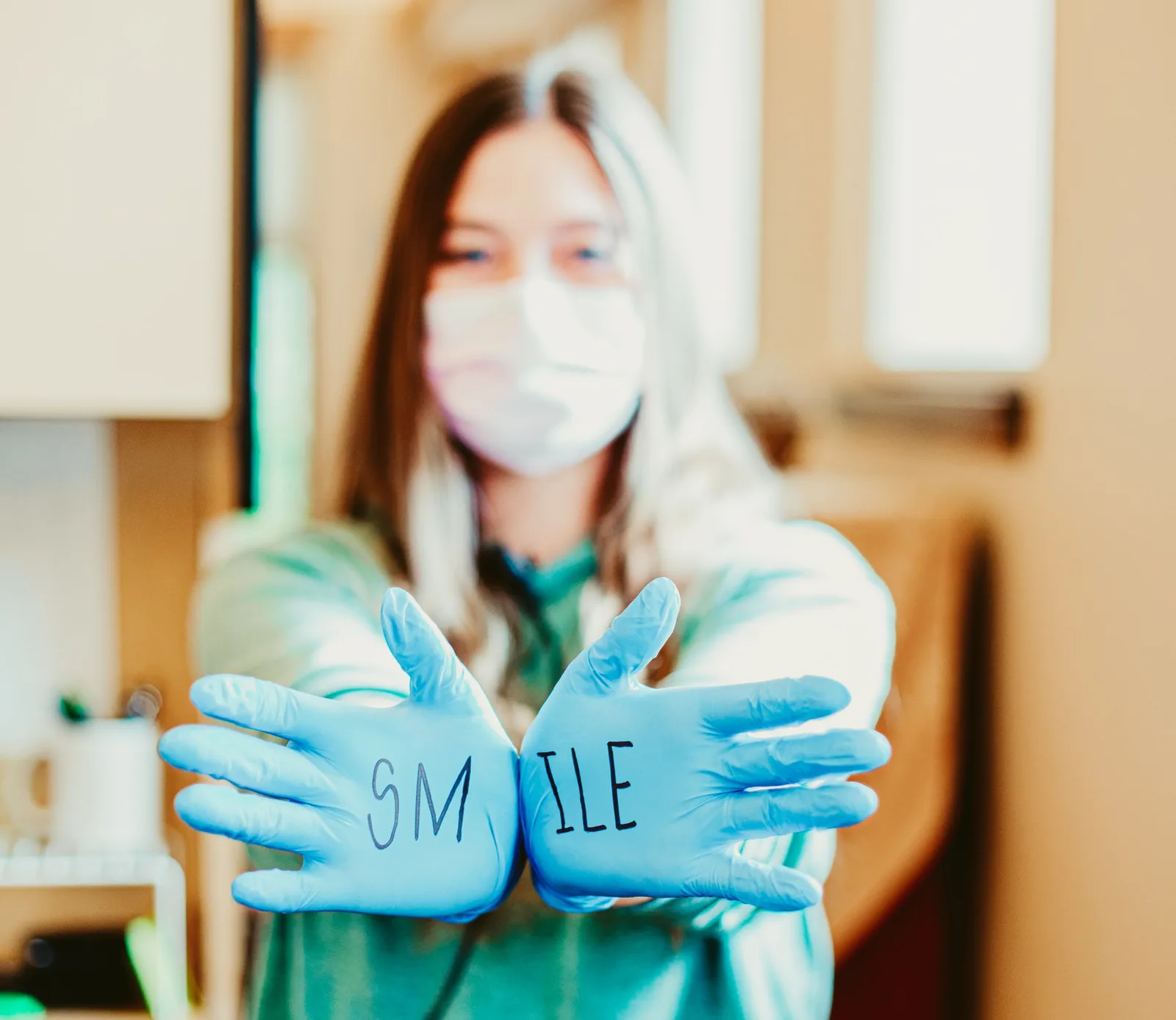 A person wearing a mask holds up blue gloves with the word "SMILE" written across the palms.